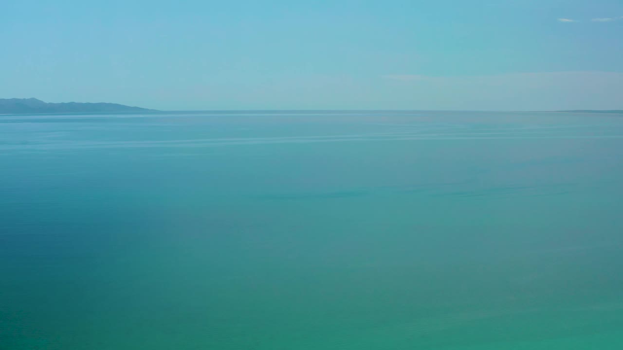 Open teal water sits beneath a pale sky in El Sargento La Ventana, Mexico, with the distant coastline slightly left of center and no visible people.