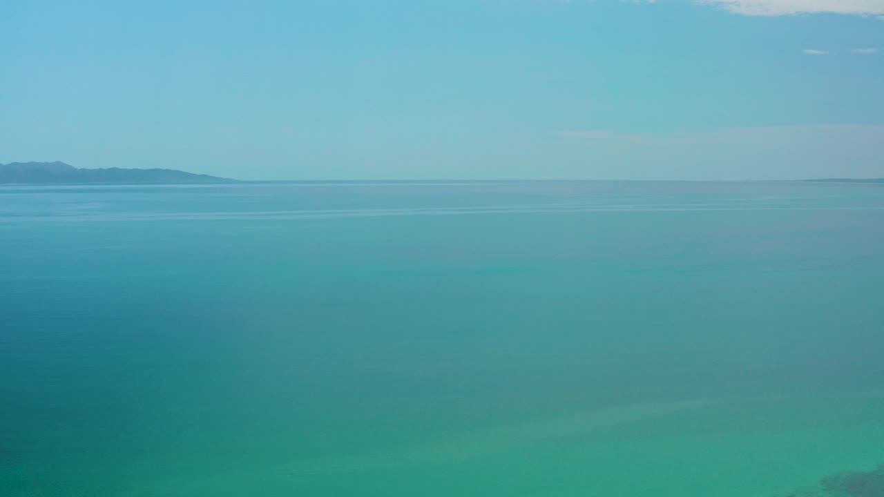 Opening frame over blue-green water near El Sargento La Ventana, Mexico, with a low distant landform on the horizon and no visible people.