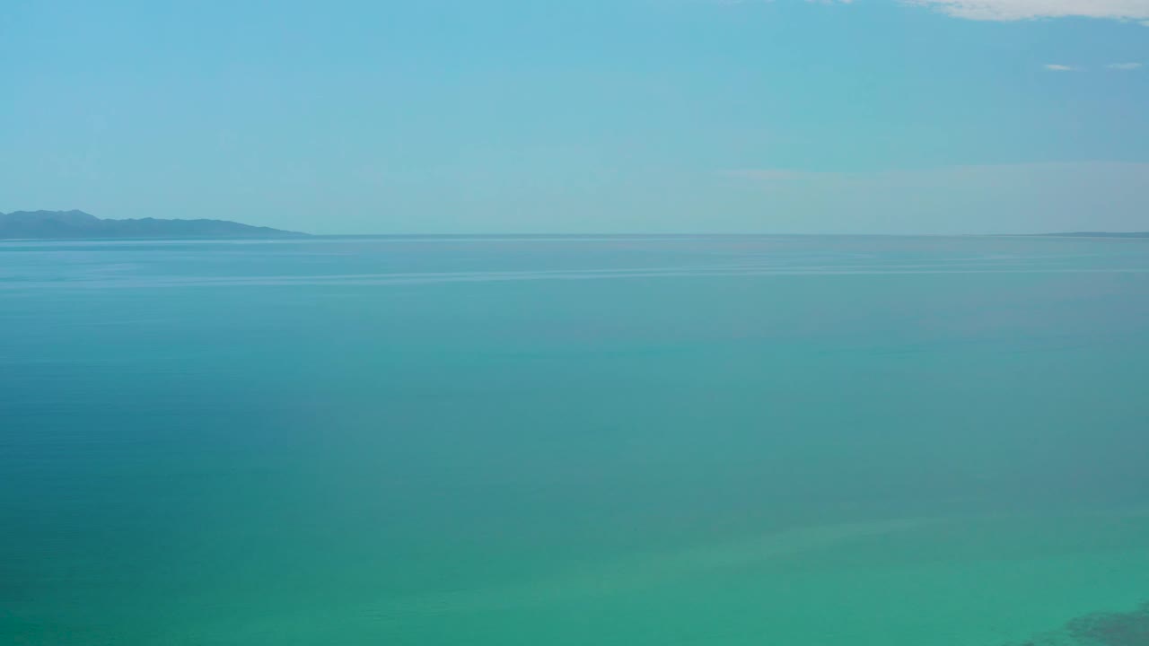 Second frame showing still turquoise water at El Sargento La Ventana, Mexico, with faint surface bands, distant land, and no visible people.