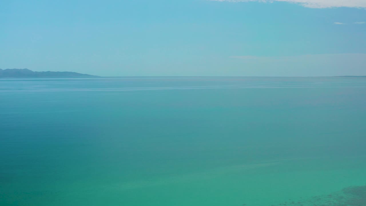 Mid-clip view over calm blue water near El Sargento La Ventana, Mexico, with the distant landform shifted toward the left horizon and no visible people.