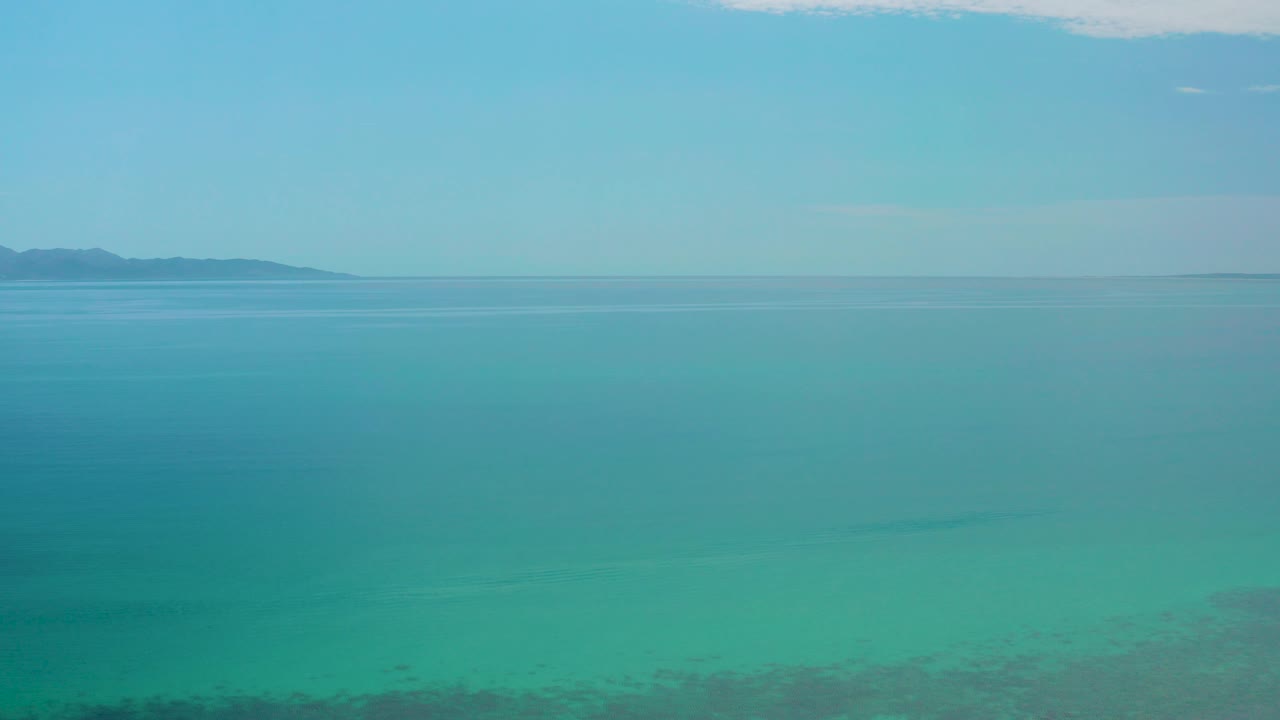 Turquoise sea under pale blue sky with distant land on the horizon.