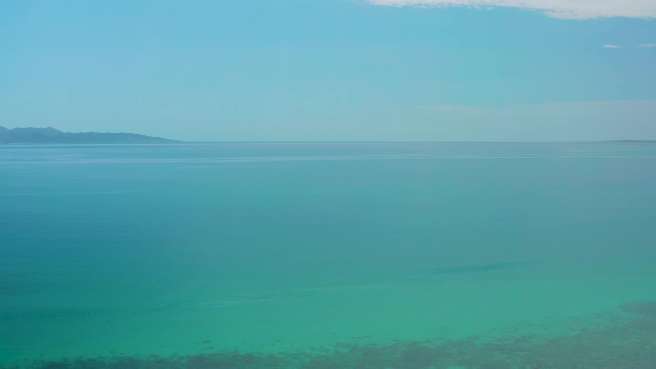 High coastal view at El Sargento La Ventana, Mexico, showing blue-green water, a small distant landform near the upper left, pale sky, and no visible people.