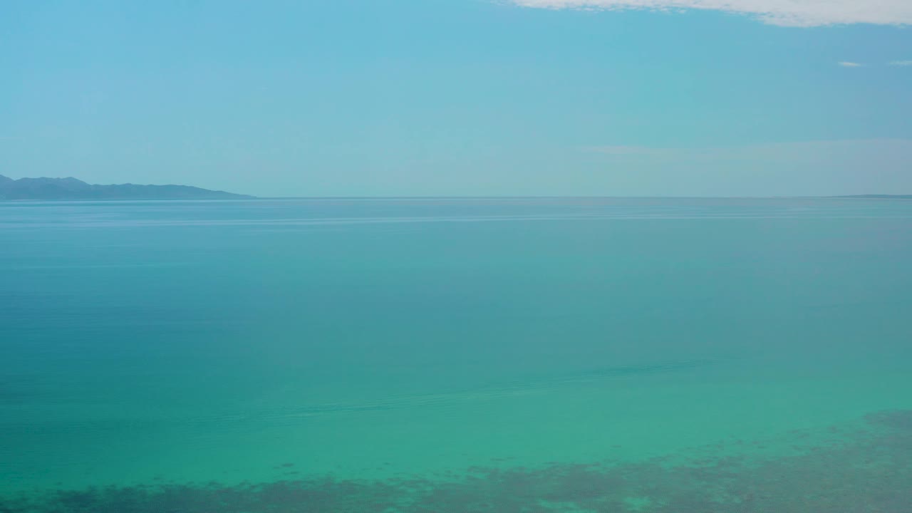 Wide view over calm turquoise water at El Sargento La Ventana, Mexico, with a thin horizon line, faint coastline at the far left, and no visible people.