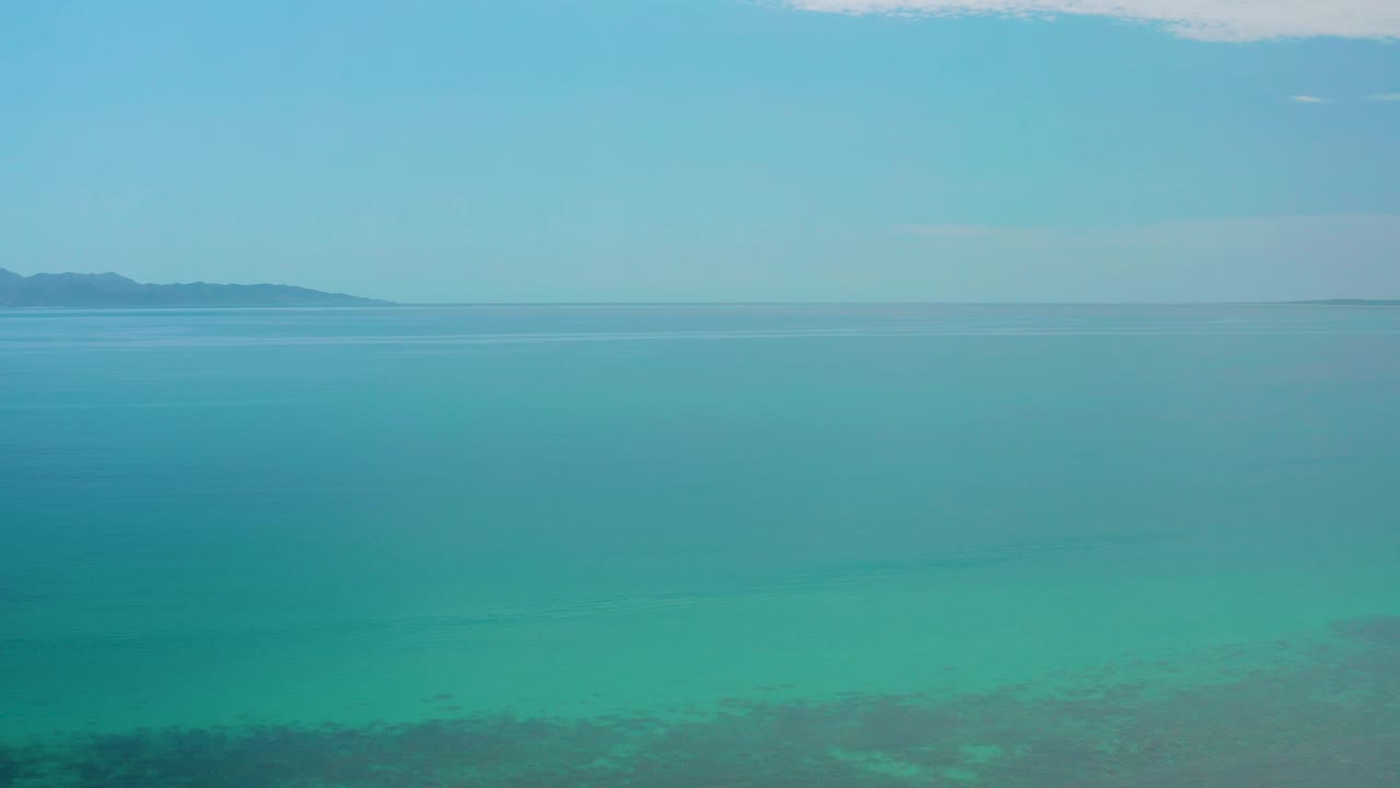 Broad high view of the El Sargento La Ventana sea, with darker shallow-water patches at the bottom, distant land along the horizon, and no visible people.