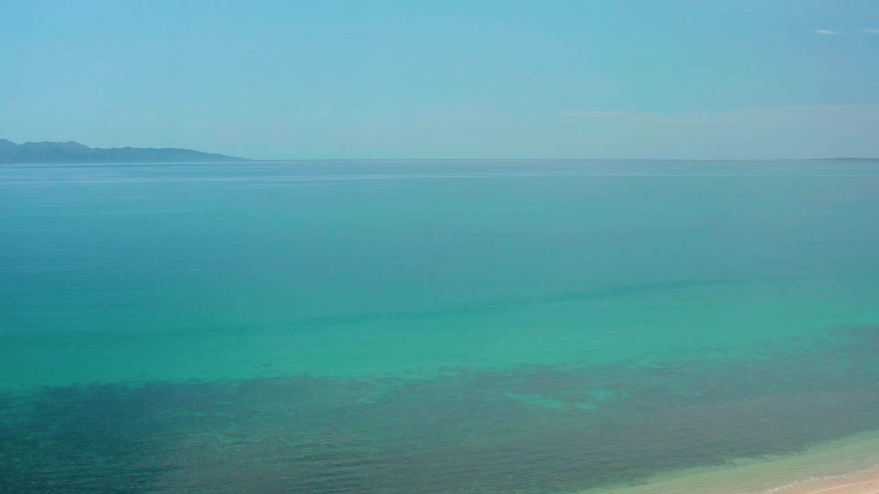 Wide aerial view of turquoise water with distant land on the horizon.