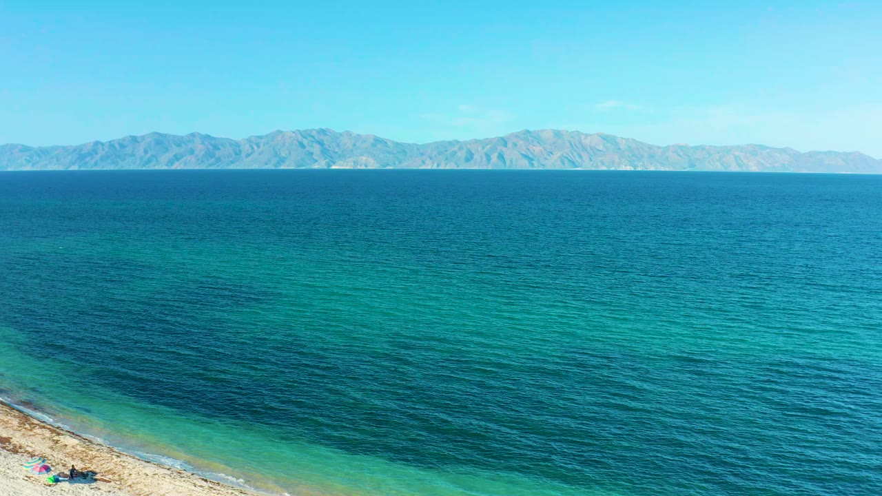 A broad band of blue and teal sea fills the frame in El Sargento La Ventana, Mexico, with the shoreline just visible at the bottom left and no visible people.