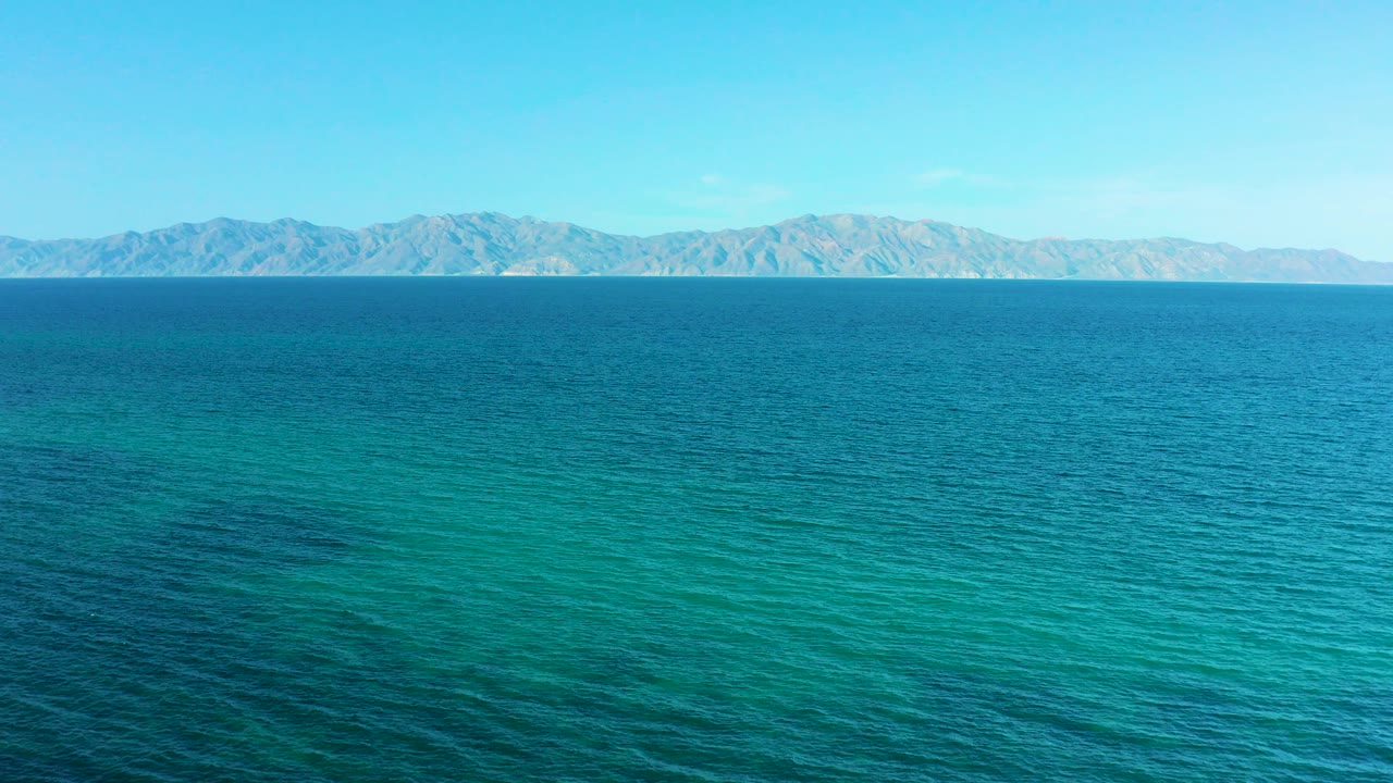 Opening frame of El Sargento La Ventana, Mexico with turquoise ocean in the foreground, distant mountains along the horizon, bright blue sky, and no visible people.