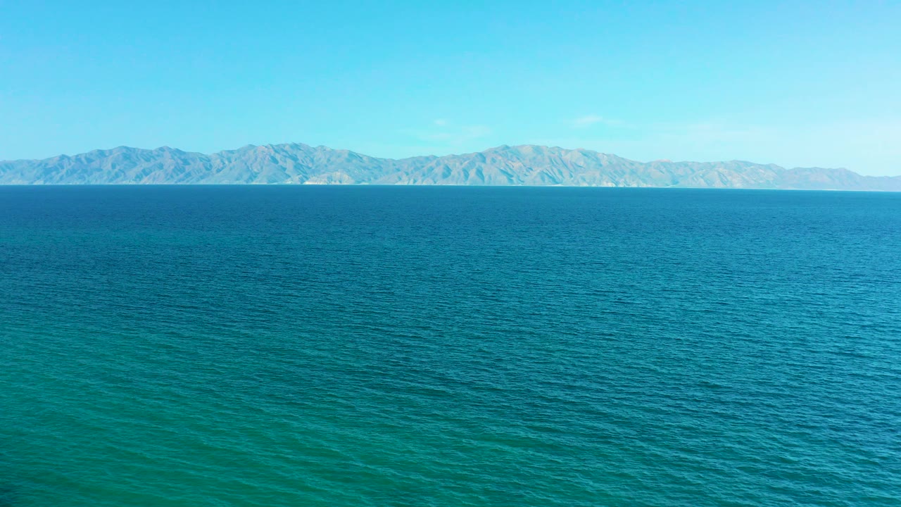 Wide aerial view of blue sea and distant mountains under a clear sky.