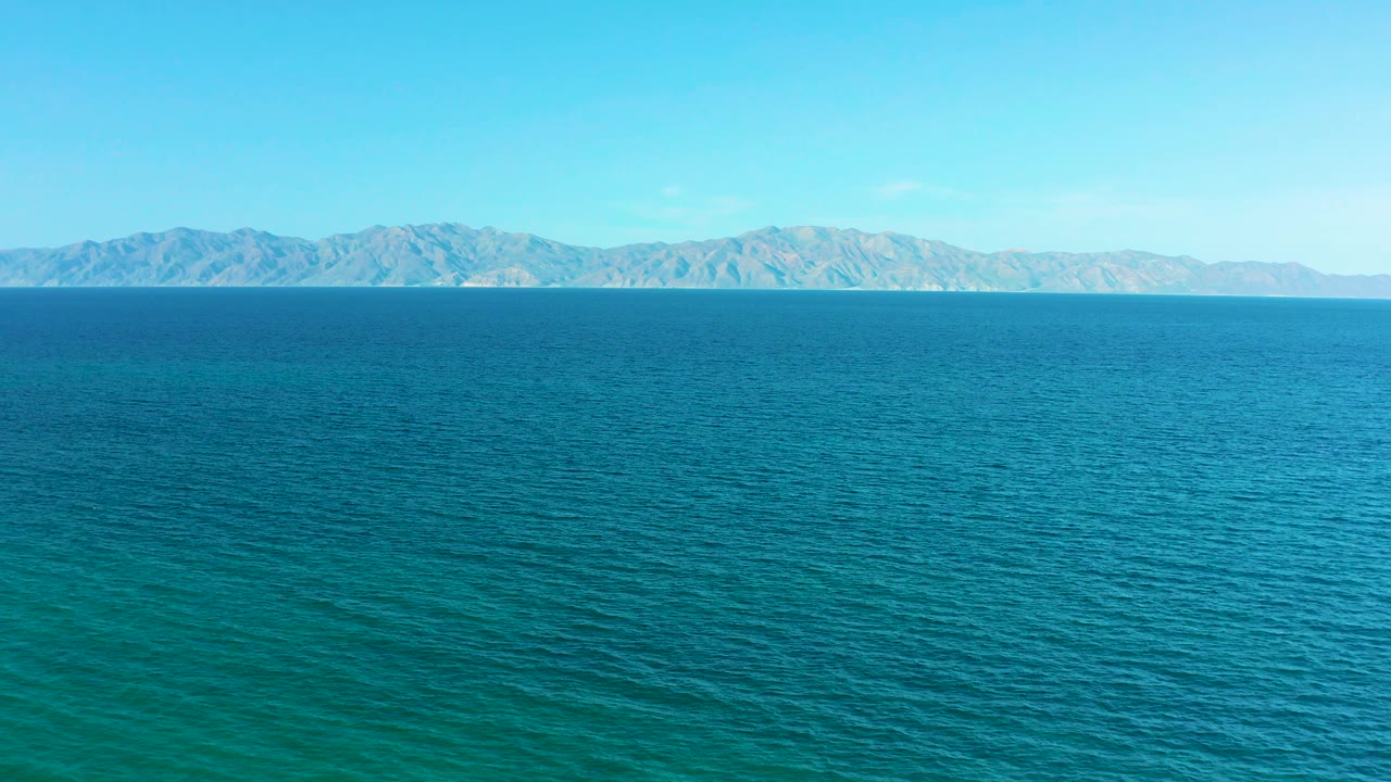 At 0:03, textured blue water dominates the aerial view, with pale mountains across the background and no visible people, boats, or buildings.