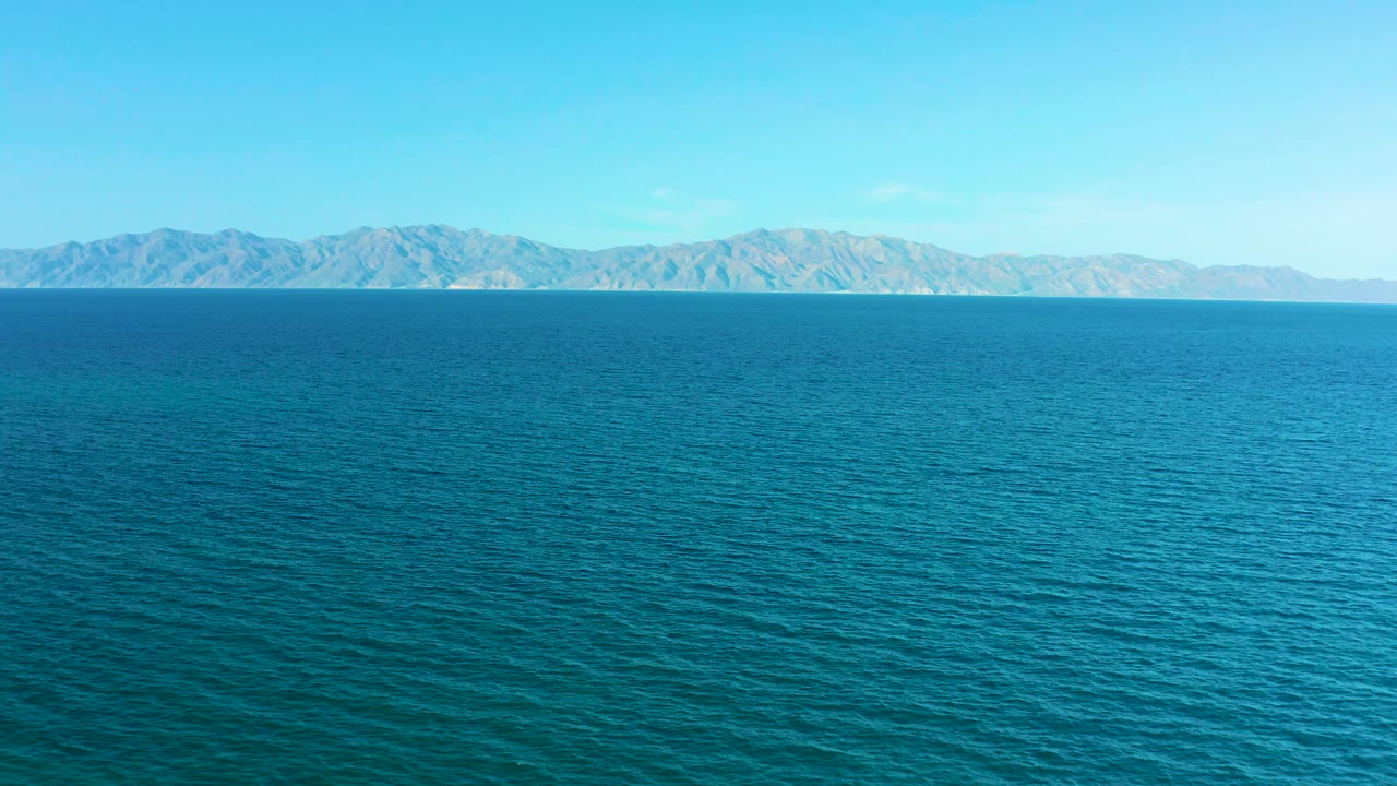 Turquoise-blue water stretches toward dry distant hills beneath a clear sky in El Sargento La Ventana, Mexico, with no visible people or vessels.