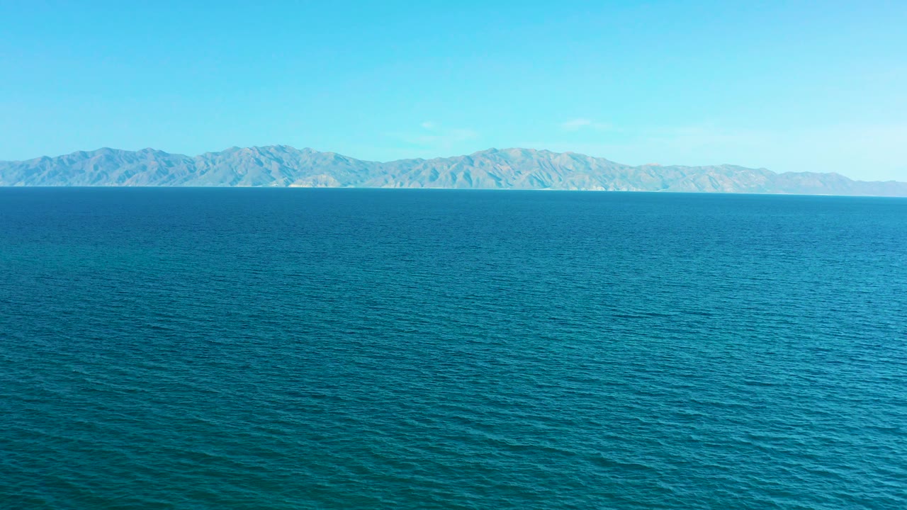 A calm blue water foreground fills the lower frame while low hills run across the background in El Sargento La Ventana, Mexico, with no visible people.