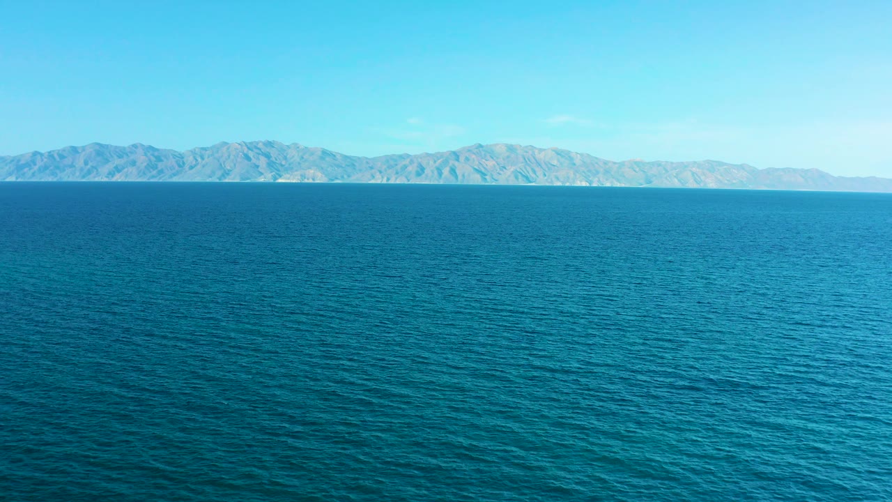 Open blue water stretches toward a rugged mountain horizon in El Sargento La Ventana, Mexico, with clear daylight and no visible people.