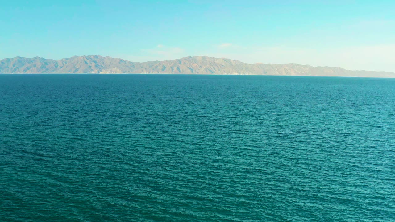 Opening frame of blue-green ocean in El Sargento La Ventana, Mexico, with a distant mountain range on the horizon and no visible people.