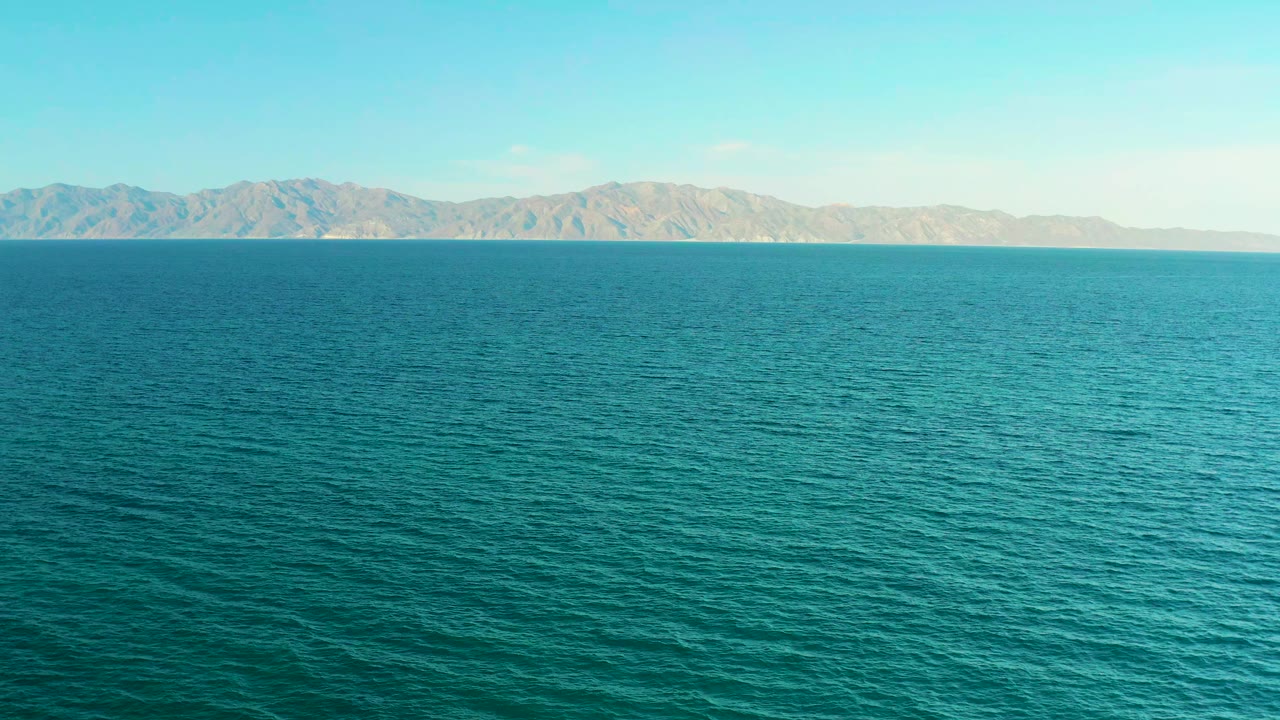 Blue-green water texture continues across the frame in El Sargento La Ventana, Mexico, with the mountain ridge slightly clearer and no visible people.