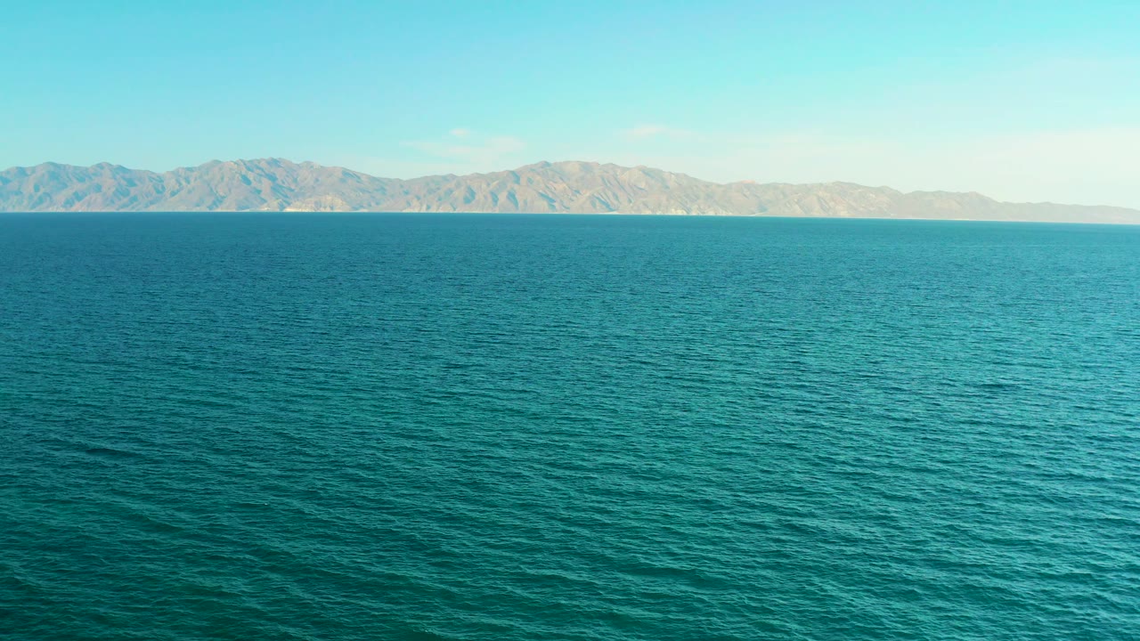 A wide 4K sea view from El Sargento La Ventana, Mexico, shows rippled blue-green water, low mountains, bright daylight, and no visible people.