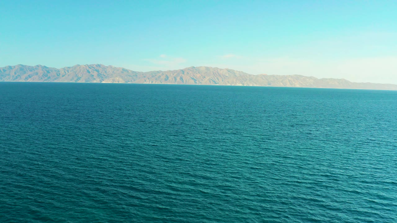 Wide view of blue water and a distant mountain range in El Sargento La Ventana, Mexico, with no visible people at the opening moment.