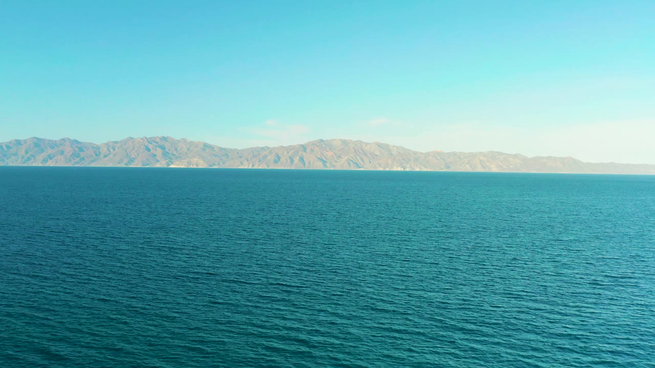 At 0:02, the frame shows turquoise-blue ocean in El Sargento La Ventana, Mexico, a continuous low mountain backdrop, clear daylight, and no visible people.