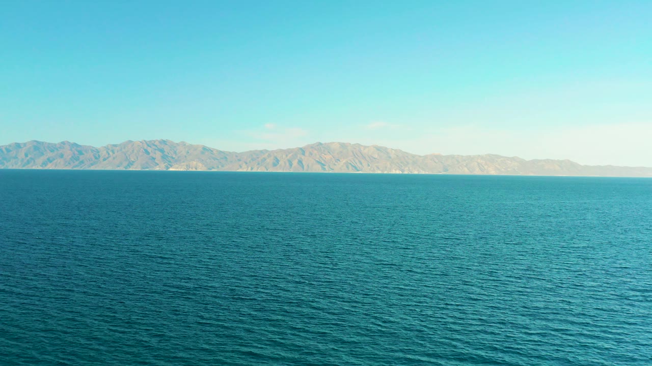 At 0:03, rippled blue ocean stretches toward a rugged tan ridge in El Sargento La Ventana, Mexico, with a clean sky and no visible people.