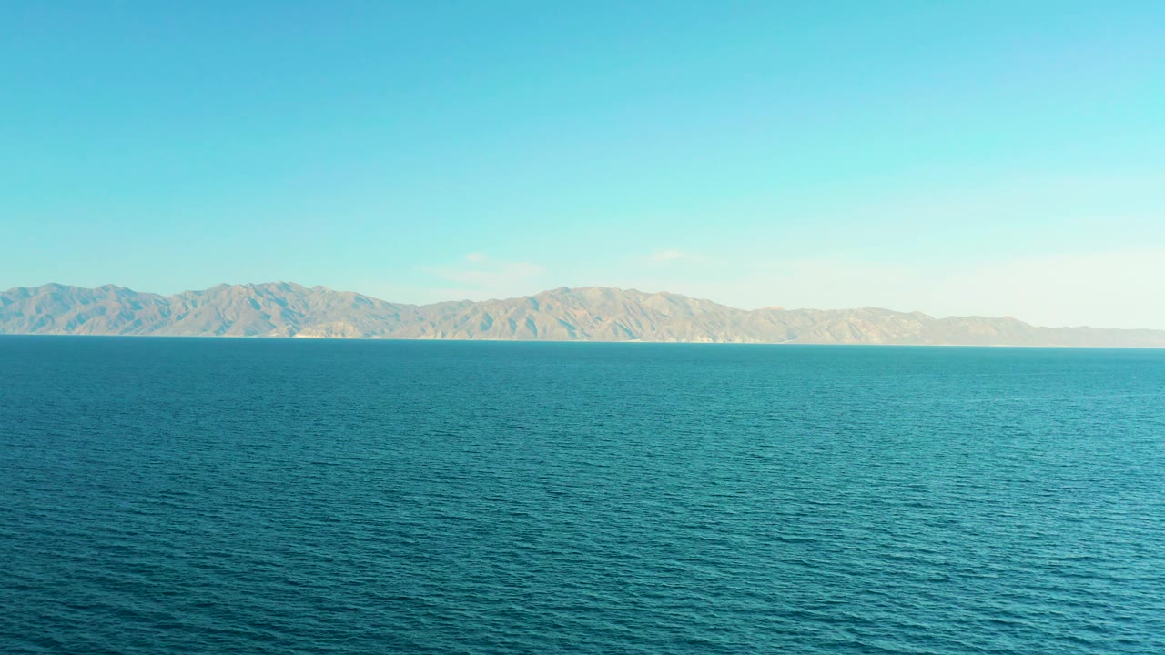 Open blue ocean faces a long mountain coastline at El Sargento La Ventana, Mexico, with clear sky overhead and no visible people.