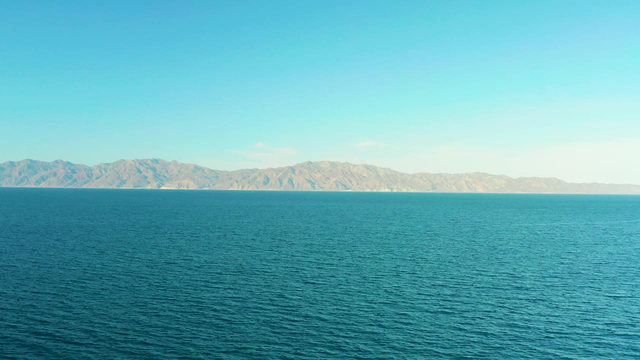 Mid-clip frame of calm blue ocean and distant brown mountains in El Sargento La Ventana, Mexico, with no visible people or vessels.