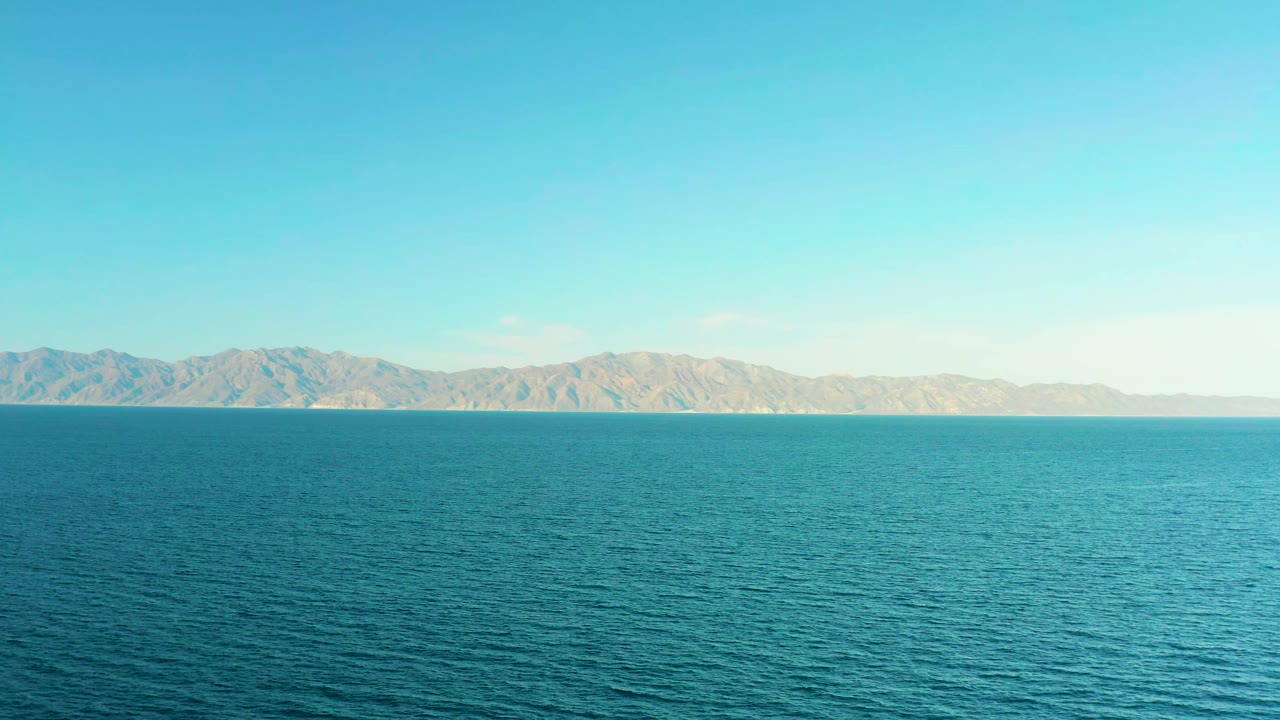 A broad view of El Sargento La Ventana, Mexico, shows rippled ocean filling most of the frame, low mountains across the background, bright daylight, and no visible people.