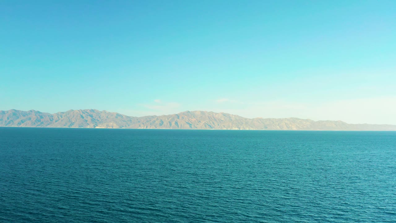 The frame presents El Sargento La Ventana, Mexico, as an open marine vista, with textured blue water in front, tan mountains in the distance, clear sky, and no visible people.