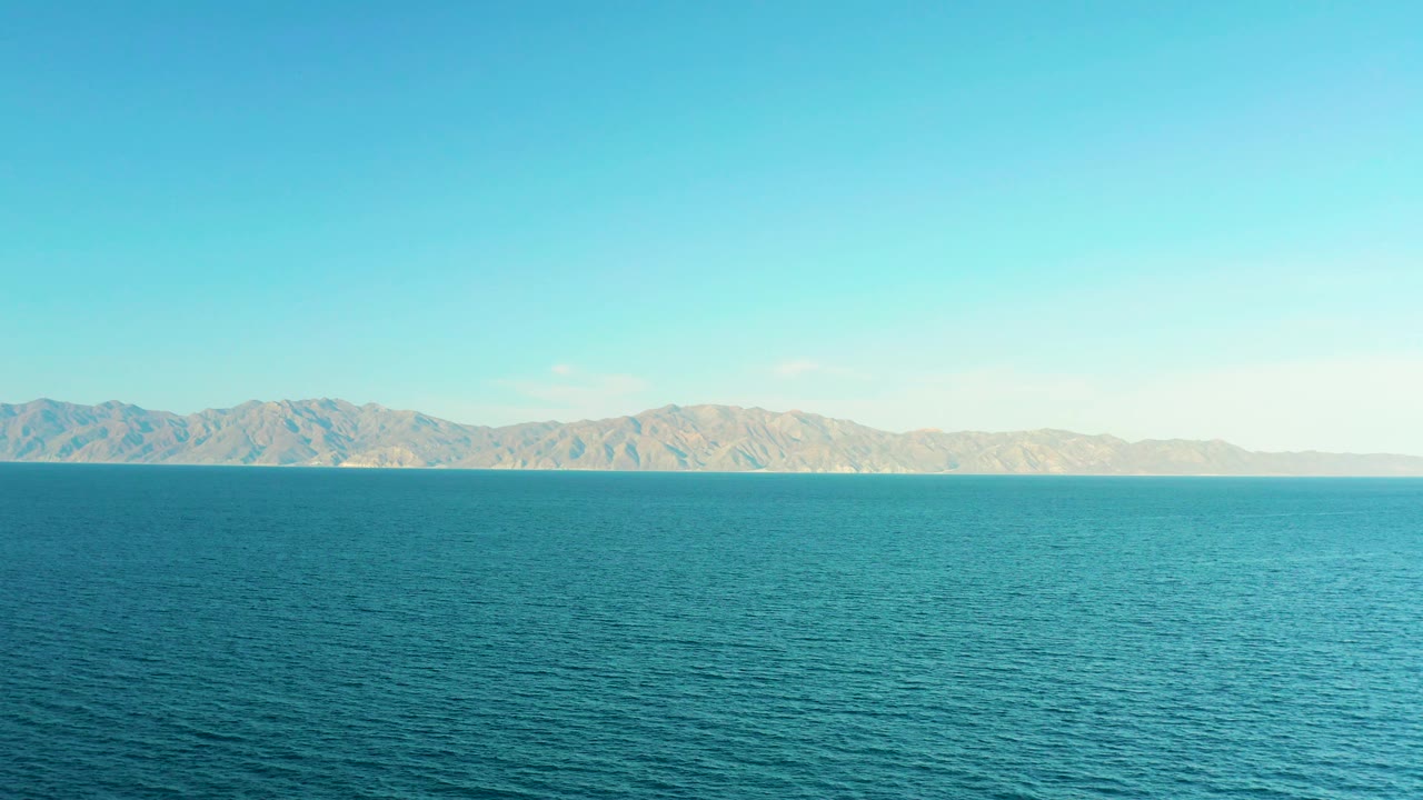 Midway through the clip, El Sargento La Ventana, Mexico, appears as a steady horizontal composition of turquoise water, a thin distant shore, pale mountains, and no visible people.