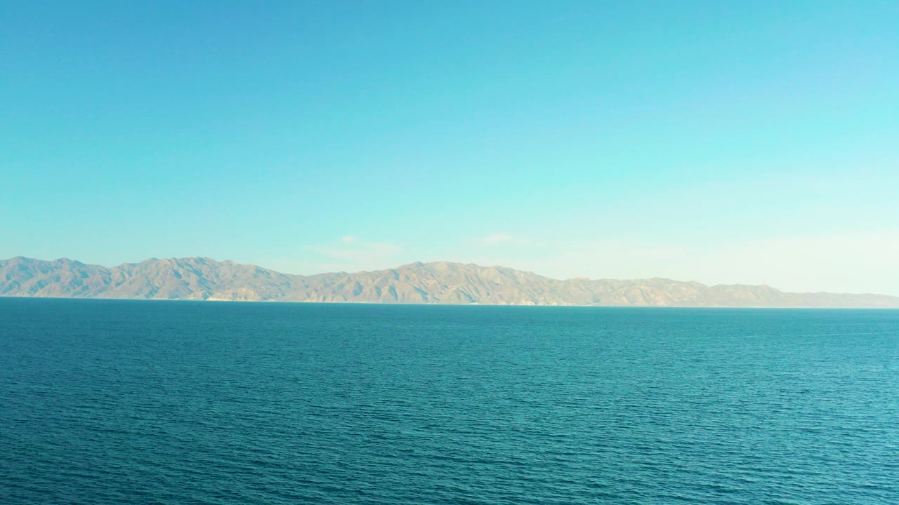 Blue ocean with distant hills under a clear sky