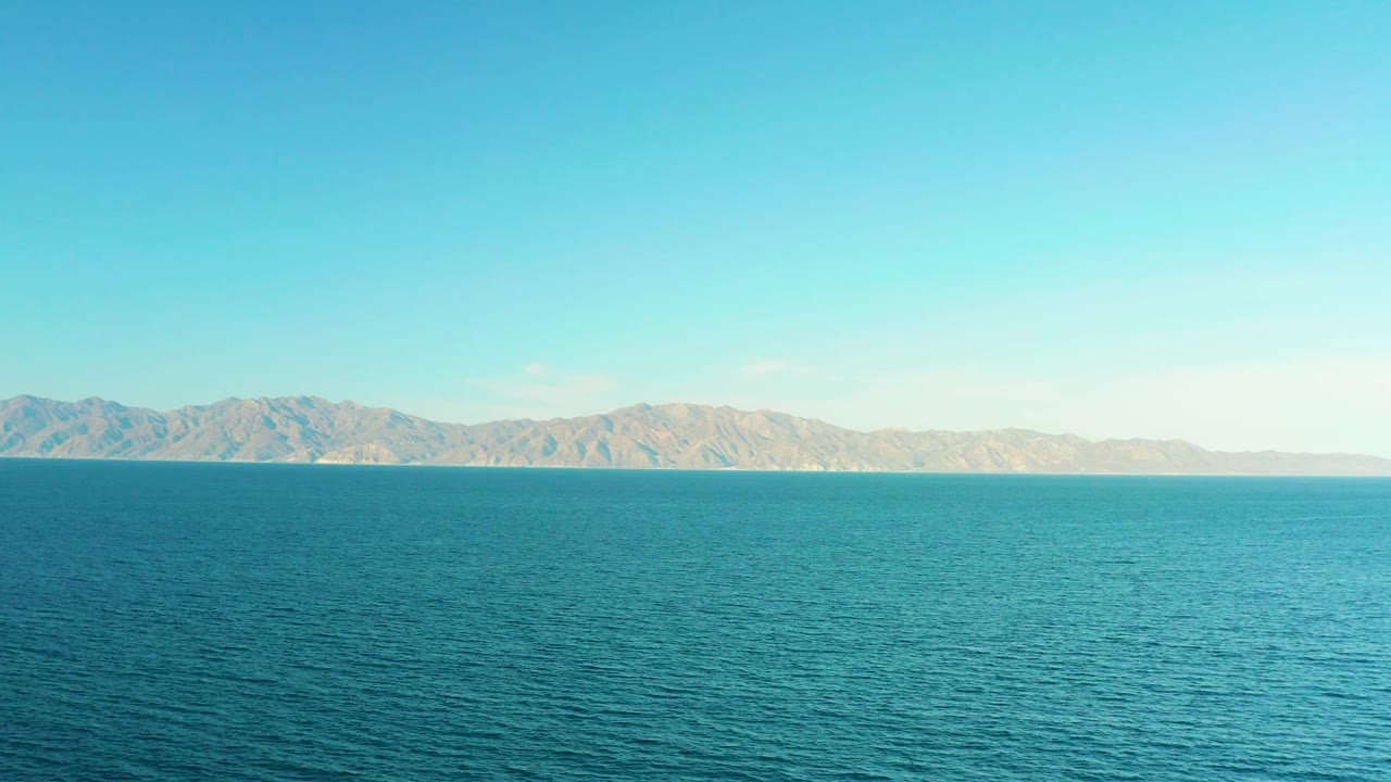 Calm blue water occupies most of the frame beneath a clear horizon and distant hills in El Sargento La Ventana, Mexico, with no visible people.
