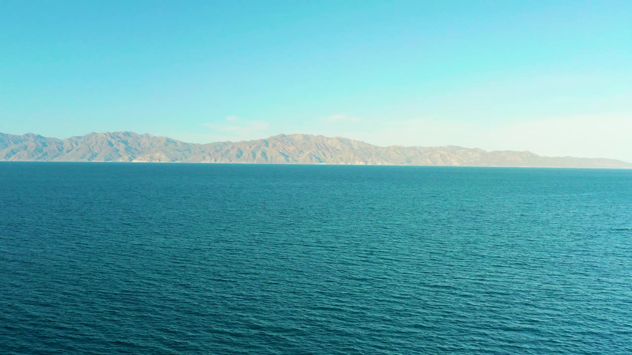 Blue water with distant mountains under a pale sky