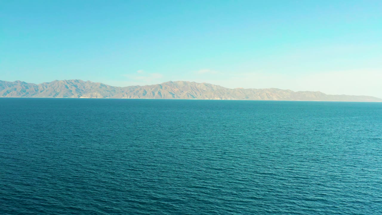 A wide section of rippled sea sits below a low mountain ridge in El Sargento La Ventana, Mexico, with bright daylight and no visible people.