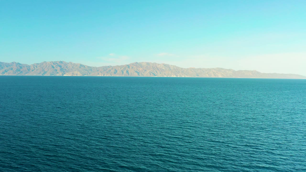 Turquoise water stretches toward tan mountains across the horizon in El Sargento La Ventana, Mexico, with clear sky and no visible people.