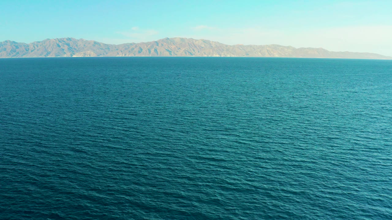 Wide view over blue ocean toward tan mountains near El Sargento La Ventana, Mexico, with no visible people or boats.