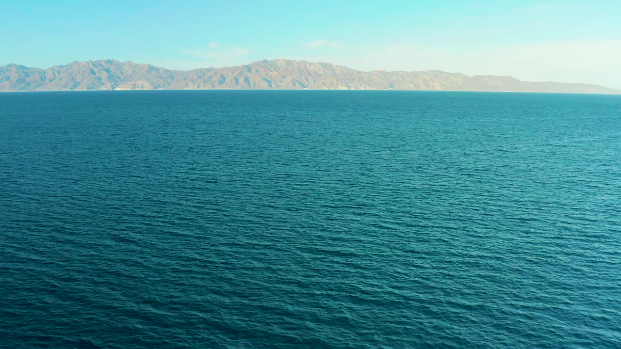 Turquoise ocean surface with mountains across the horizon.
