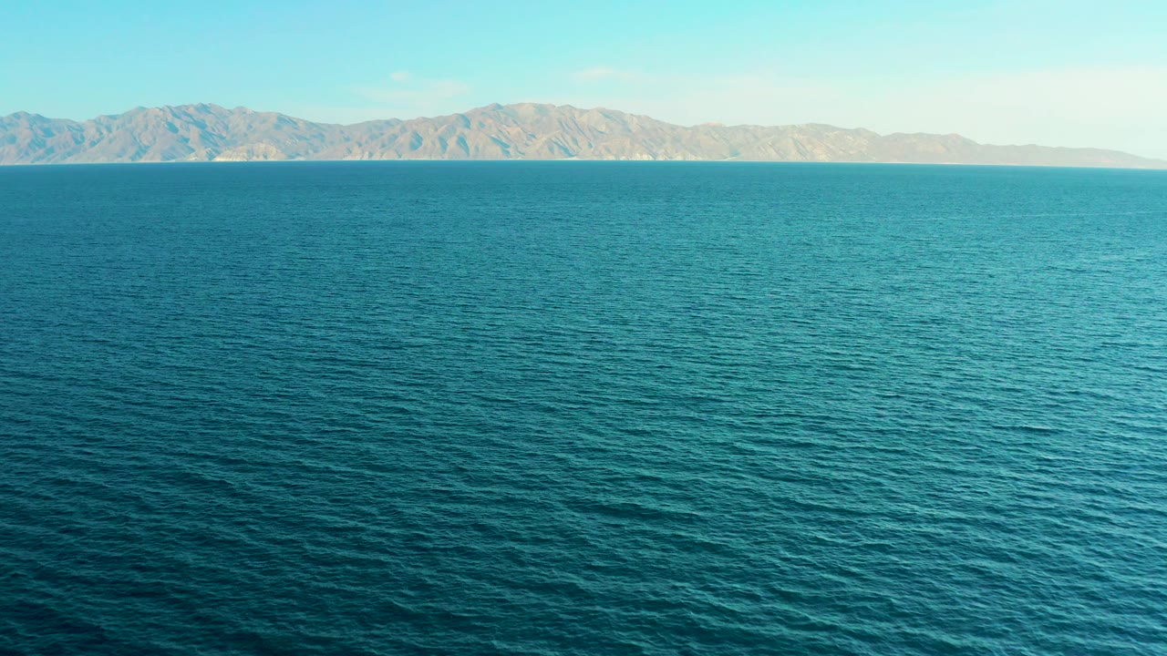 Open blue sea stretches to a distant arid mountain backdrop near El Sargento La Ventana, Mexico, with no visible people or structures.