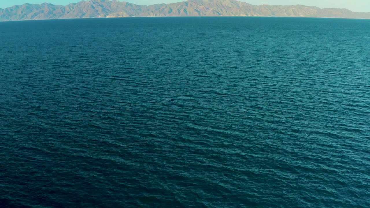 Blue ocean surface stretches toward rugged distant mountains at El Sargento La Ventana, Mexico, with no visible people or vessels.
