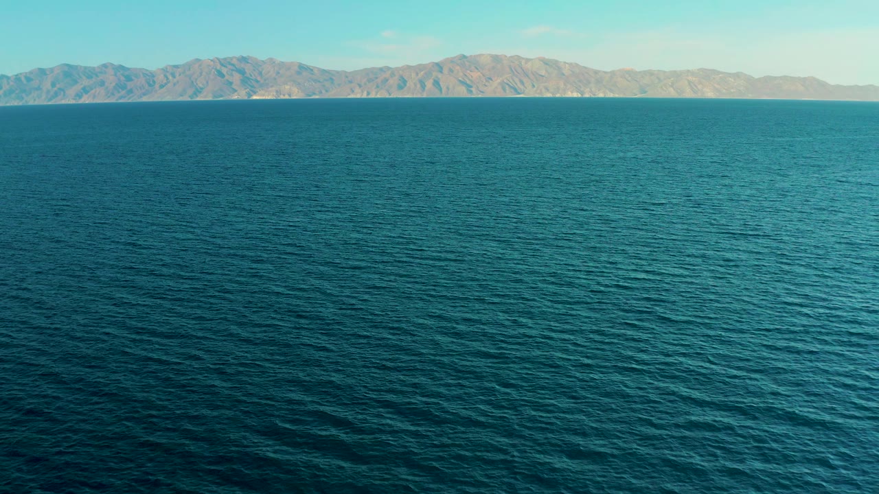 At 0:00, a wide view of blue water faces the mountain skyline of El Sargento La Ventana, Mexico, with no visible people.