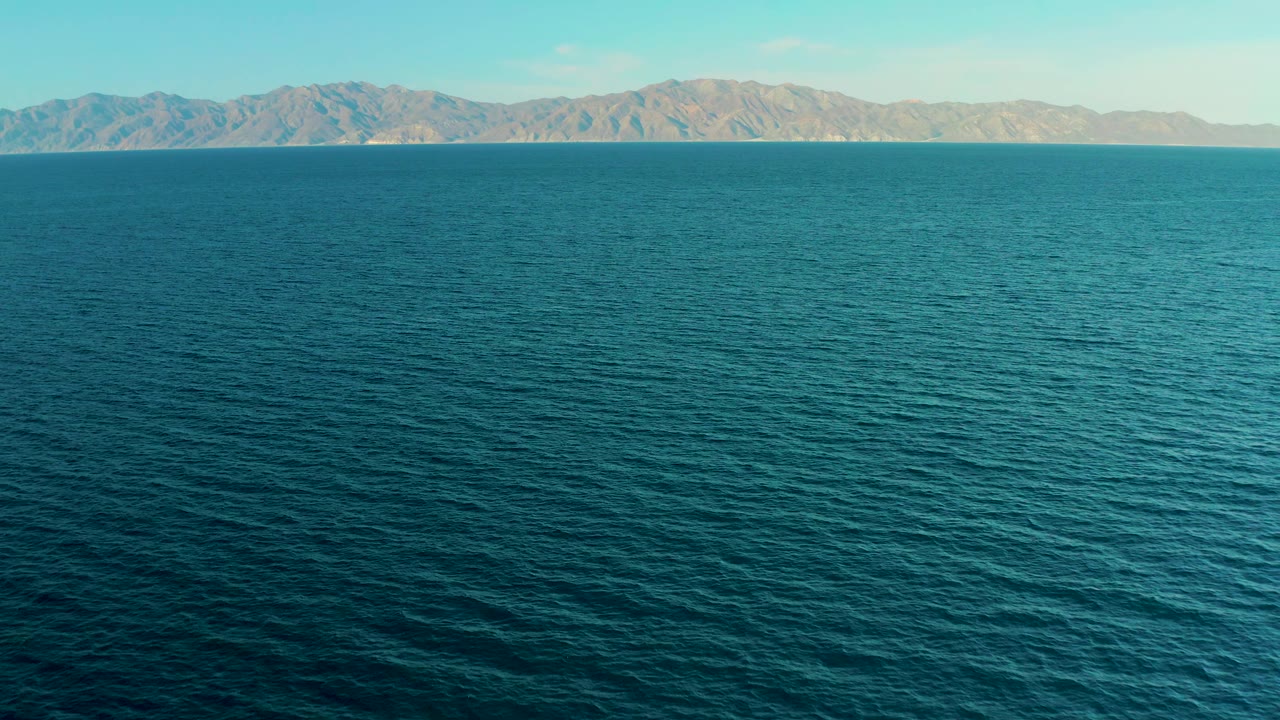 At 0:01, the ocean surface remains dominant while the distant mountain range sits evenly across the horizon in El Sargento La Ventana, Mexico, with no visible people.