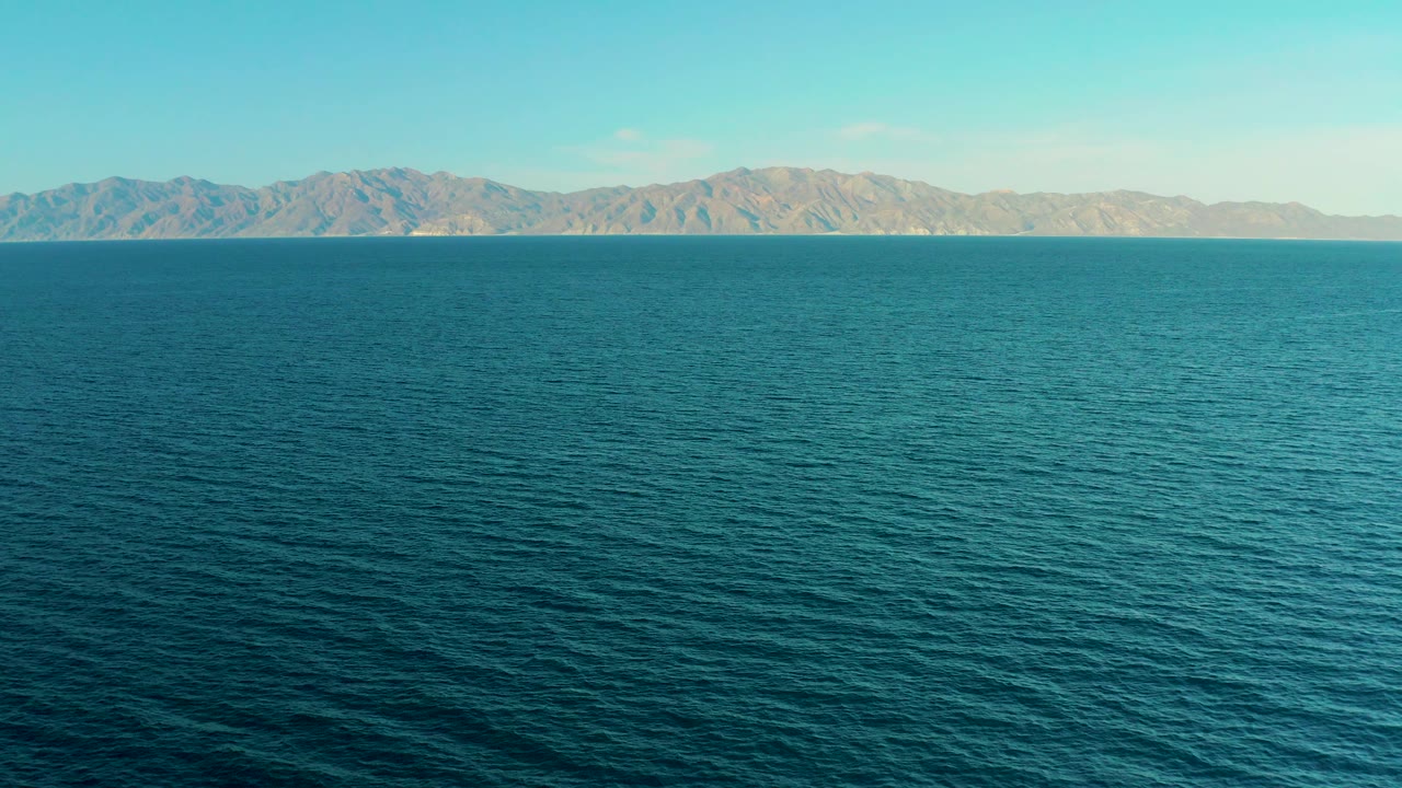 Wide ocean surface with distant mountains under clear sky