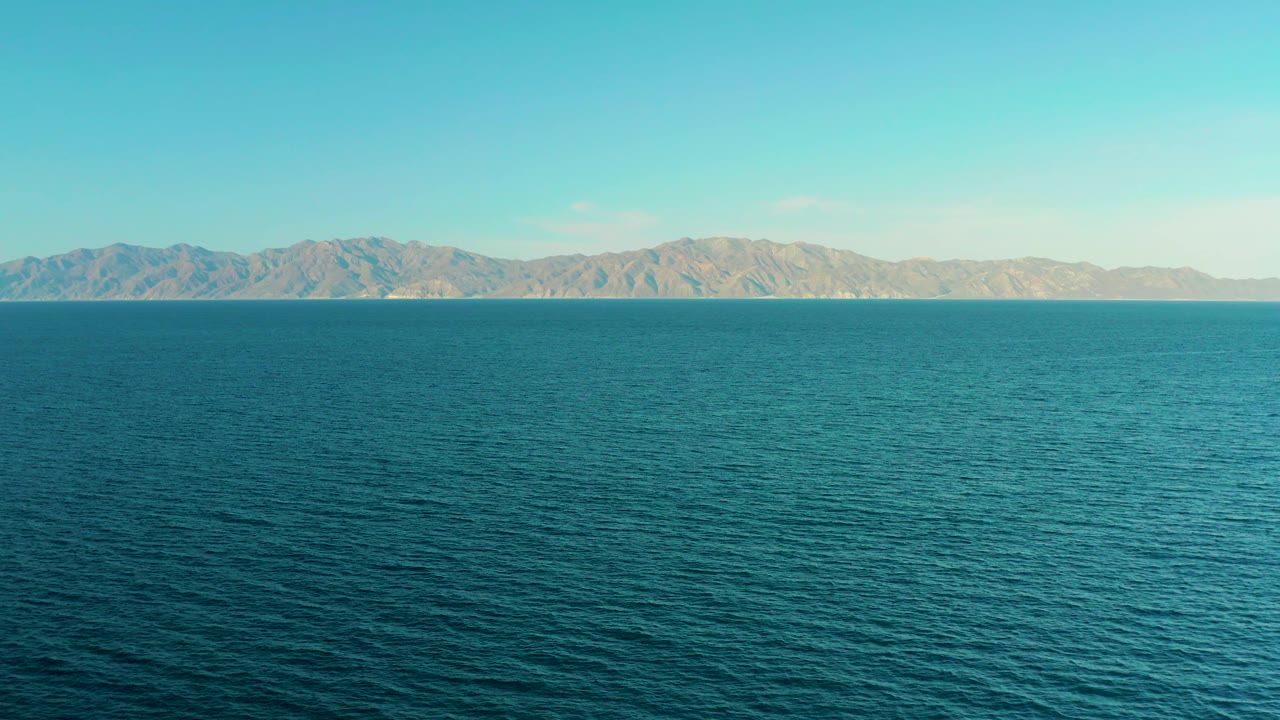 Opening frame of blue water facing distant tan mountains in El Sargento La Ventana, Mexico, with a level horizon and no visible people.
