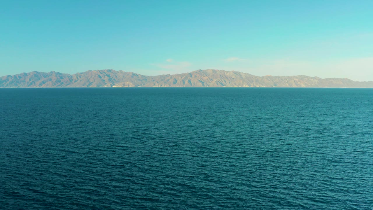 Early frame showing textured blue water in the foreground and a continuous mountain coastline across El Sargento La Ventana, Mexico, with no visible people.