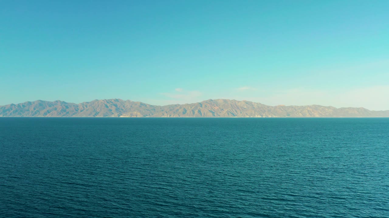Opening frame of El Sargento La Ventana, Mexico, with rippling blue water across the foreground, a distant tan mountain range on the horizon, bright sky, and no visible people.