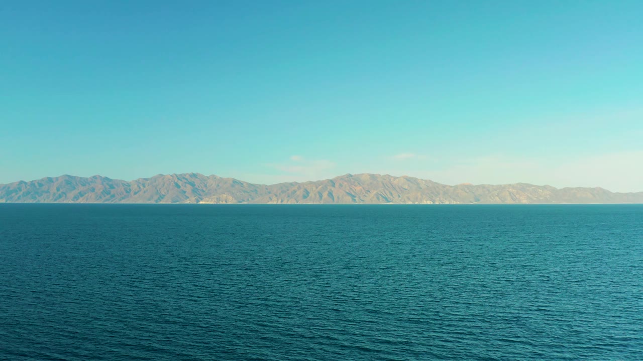 At 0:03, the frame shows a slightly lower mountain line across the distant horizon, textured blue water below, a large open sky above, and no visible people in El Sargento La Ventana, Mexico.