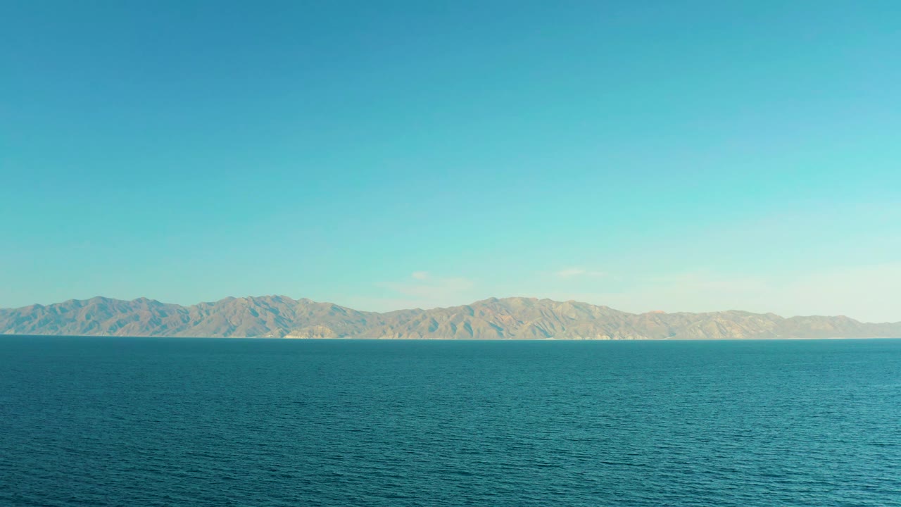 At one second, blue-green water fills the foreground while low tan mountains stretch across the horizon in El Sargento La Ventana, Mexico, with no visible people.