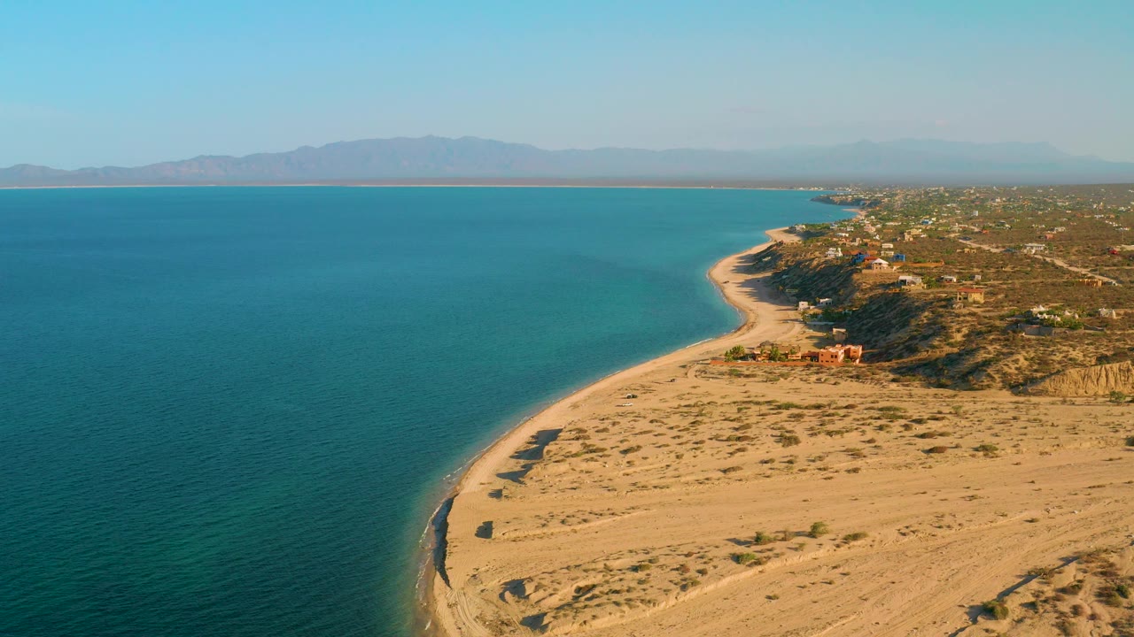 Wide aerial coastline with calm ocean and sandy point in warm light.