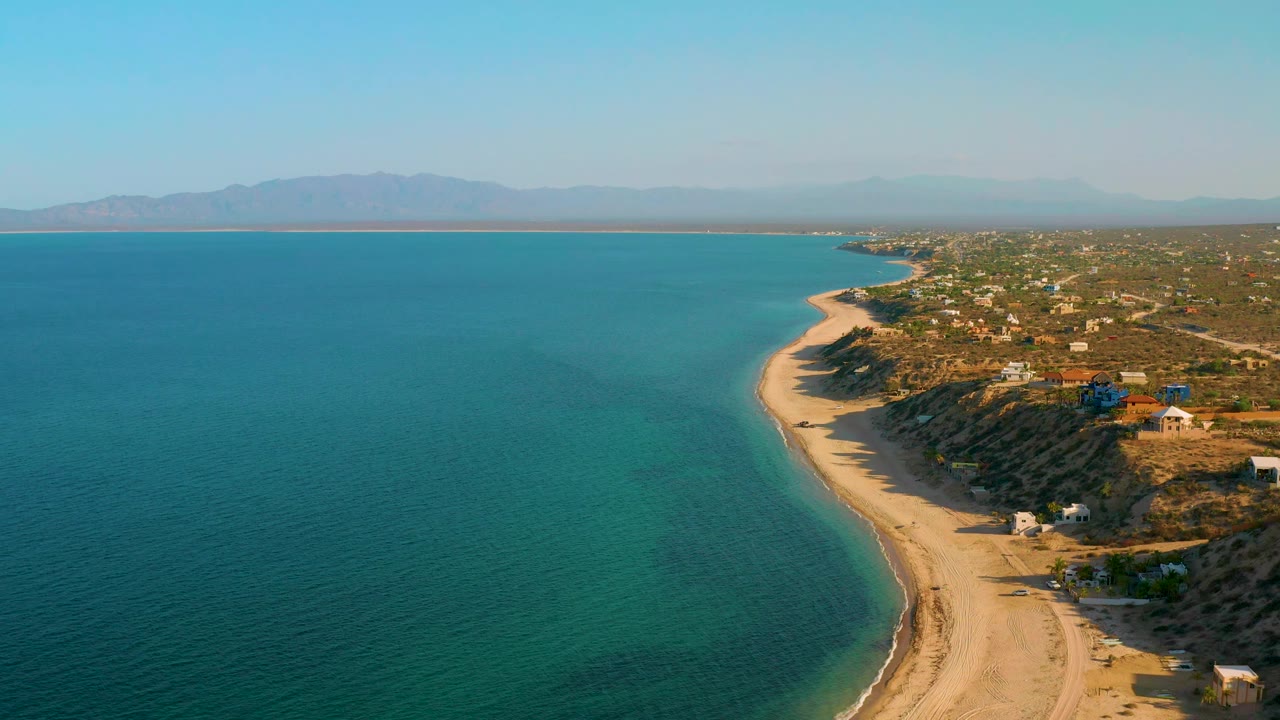 Wide drone view of turquoise bay water beside a curving sandy shoreline.