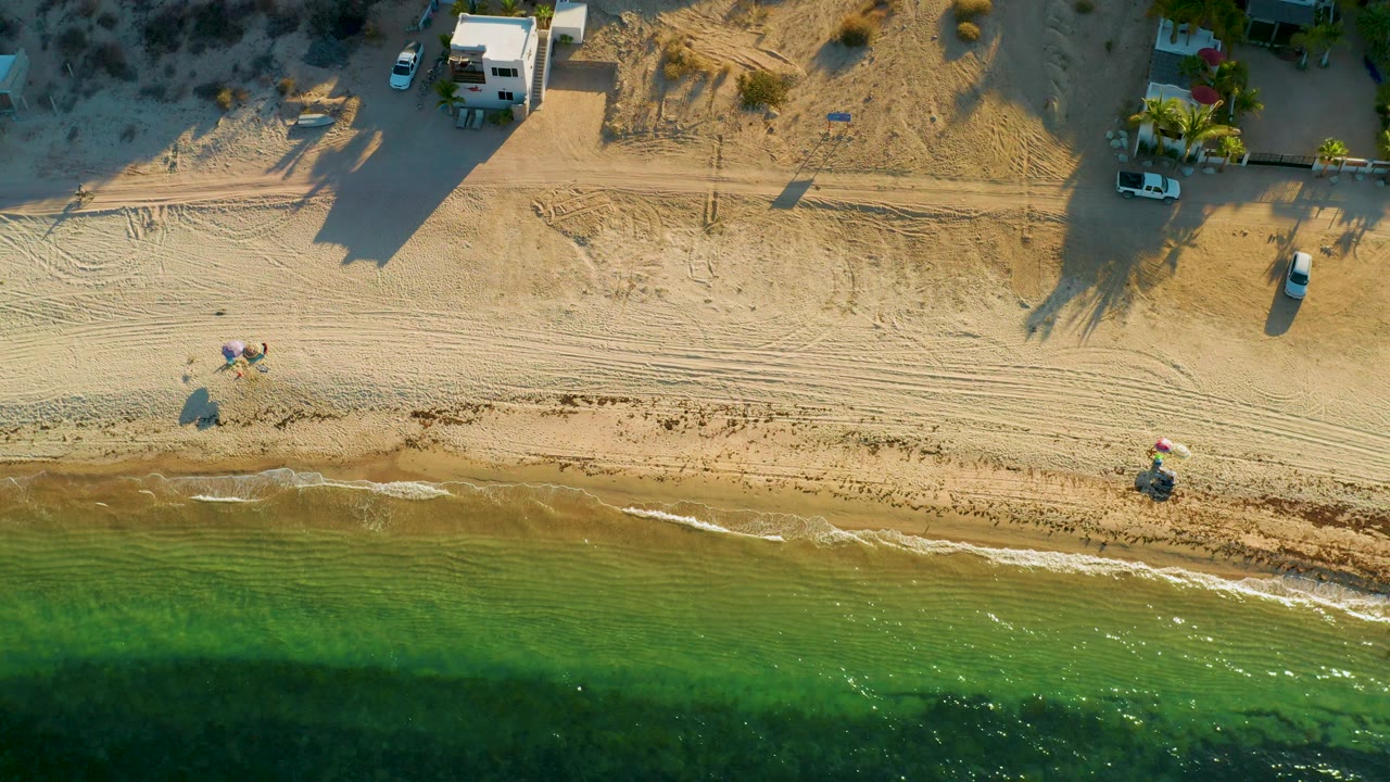 Drone-style beach view with long shadows, sand tracks, and green water
