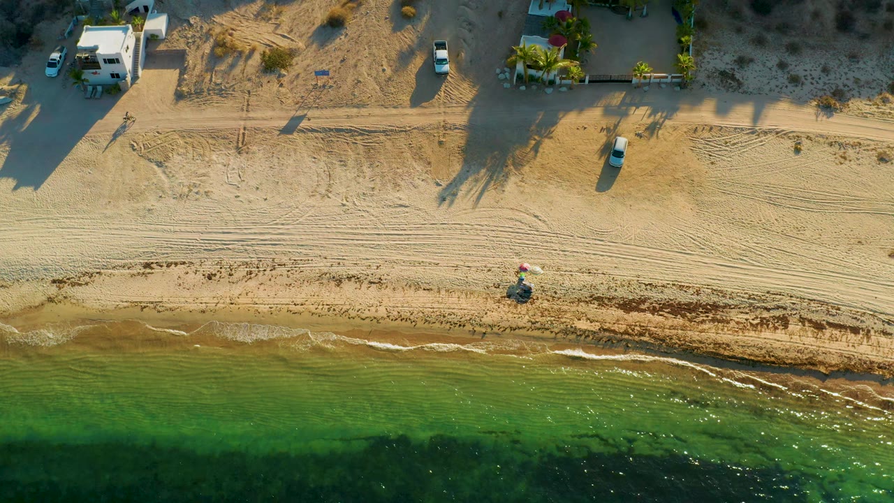 Aerial shoreline with clear green water and sandy beach tracks