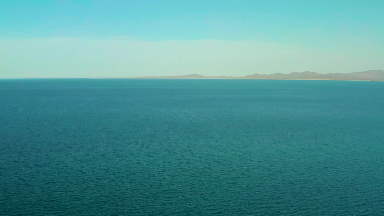 Open turquoise water fills most of the frame with a low mountain range across the horizon in El Sargento La Ventana, Mexico, and no visible people.