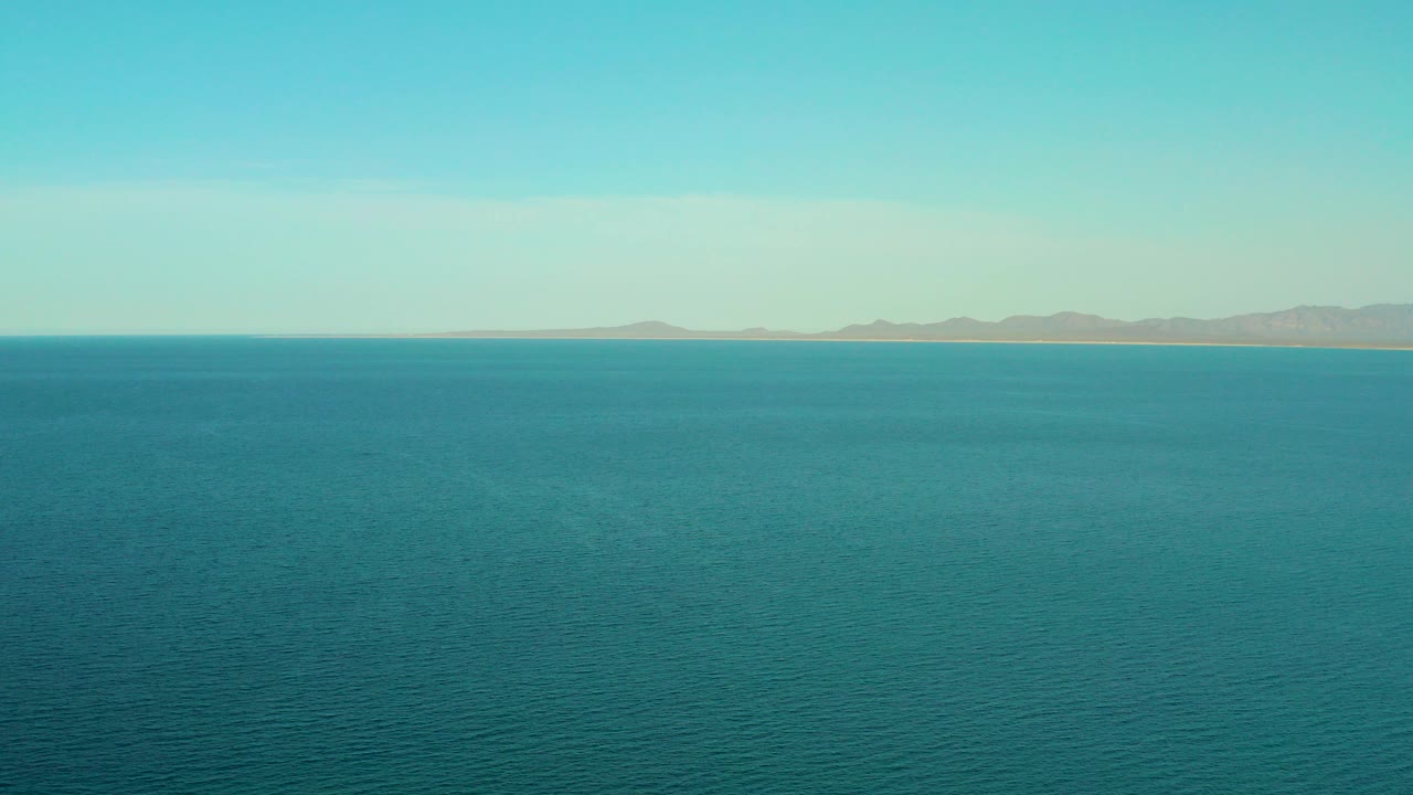 Blue ocean under a pale sky with distant mountains on the horizon.